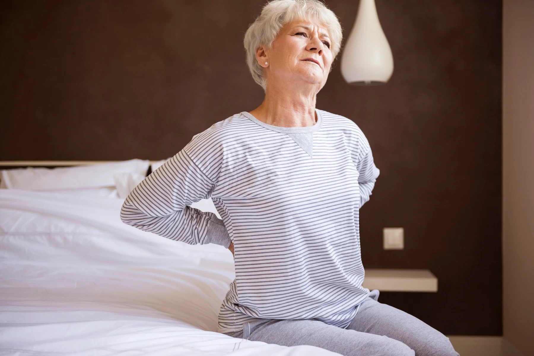 Woman seated on a bed holding her lower back